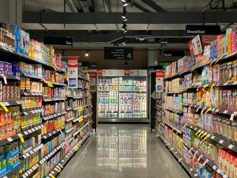 A stocked grocery aisle leading to a lit refrigerator wall